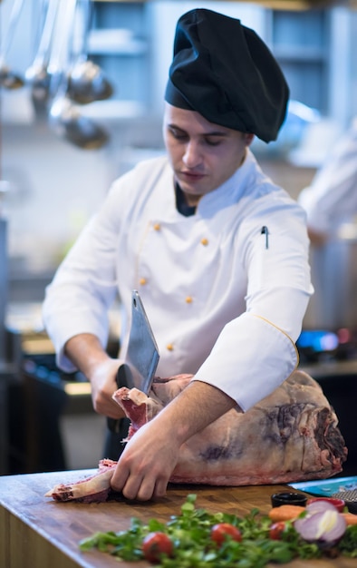 chef-kok die bijl gebruikt terwijl hij een groot stuk rundvlees snijdt op een houten bord in de keuken van het restaurant