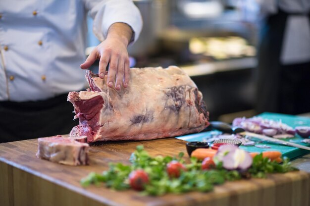 chef-kok die bijl gebruikt terwijl hij een groot stuk rundvlees snijdt op een houten bord in de keuken van het restaurant