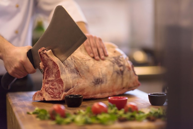 chef-kok die bijl gebruikt terwijl hij een groot stuk rundvlees snijdt op een houten bord in de keuken van het restaurant