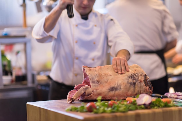 chef-kok die bijl gebruikt terwijl hij een groot stuk rundvlees snijdt op een houten bord in de keuken van het restaurant