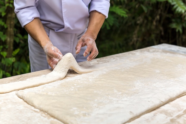 Chef-kok die deeg in keuken in de tuin met groen blad op achtergrond voorbereiden