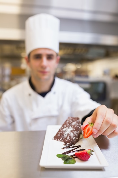 Chef-kok die een aardbei op dessertplaat zet