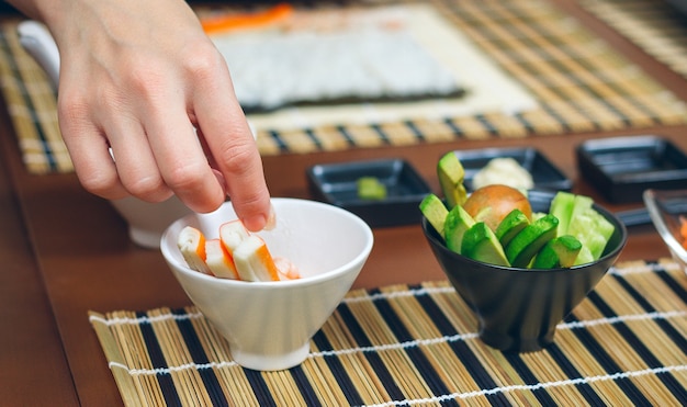 Chef-kok die een krabstok neemt van de ingrediënten die zijn bereid om sushi te maken