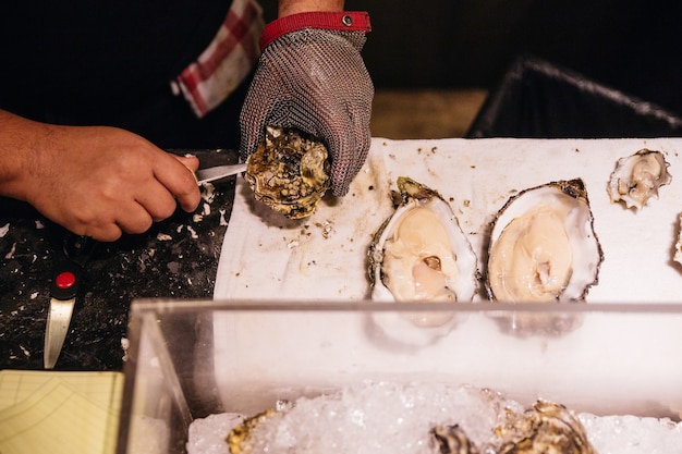 Chef-kok die een verse oester met mes en roestvrij staal gaasoesterhandschoen plakt