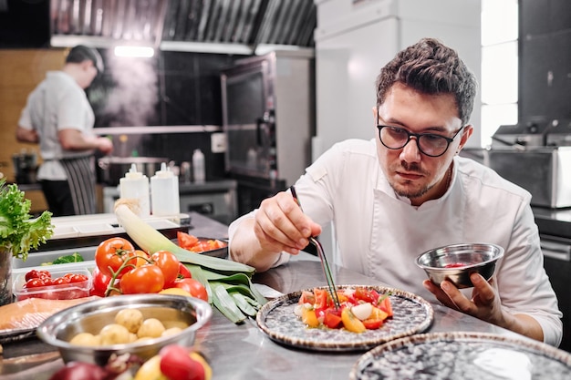 Chef-kok die groente in schotel op plaat toevoegt