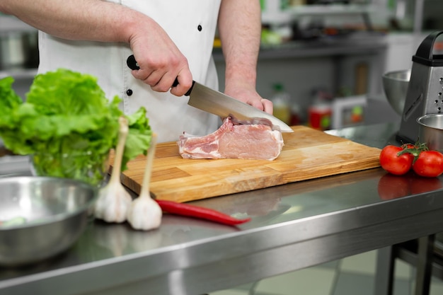 Chef-kok die het vlees op een houten bord snijdt