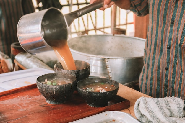 Chef-kok die Lurik-uniform gebruikt en een soep giet in soto bathok in Yogyakarta