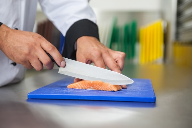 Chef-kok die ruwe zalm met mes snijdt op blauwe scherpe raad