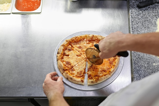 Chef-kok die versgebakken pizza snijdt met een rond mes op een houten bord. Mens die smakelijke Italiaanse gebakjeclose-up snijdt