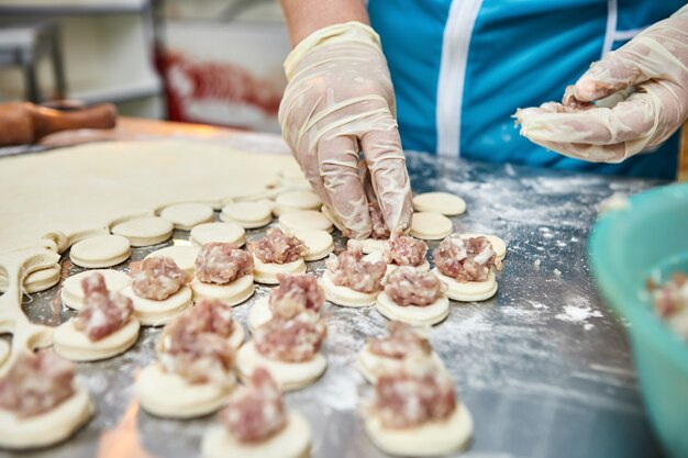 Chef-kok handen beeldhouwen knoedels op de achtergrond van snijplanken met handgemaakte, ravioli en khinkali bestrooid met bloem op een tafel. Heerlijke zelfgemaakte gerechten.