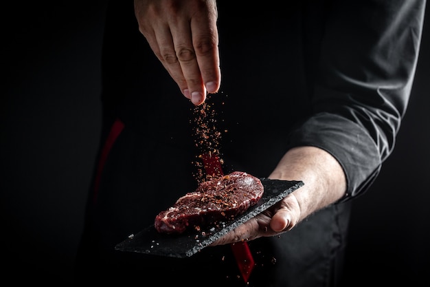 Chef-kok handen koken vlees steak en kruiden toe te voegen in een vriesbeweging. Verse rauwe Prime Black Angus beef rumpsteak. banner, menurecept.