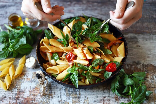 Chef-kok handen mengen pasta met groenten en basilicum.