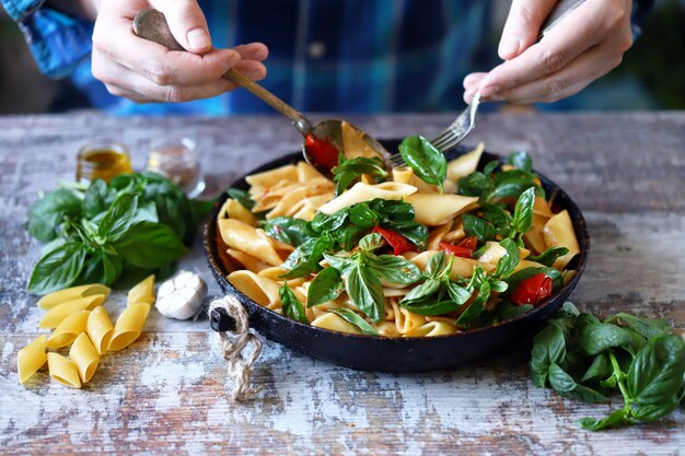 Chef-kok handen mengen pasta met groenten en basilicum.