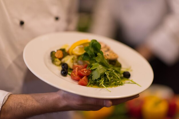 Chef-kok handen met gebakken zalm visfilet met groenten voor het diner in de keuken van een restaurant