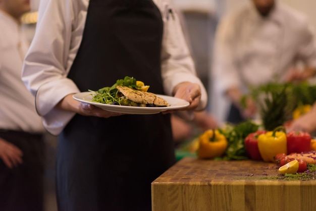 Chef-kok handen met gebakken zalm visfilet met groenten voor het diner in de keuken van een restaurant