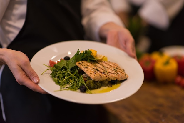 Chef-kok handen met gebakken zalm visfilet met groenten voor het diner in de keuken van een restaurant