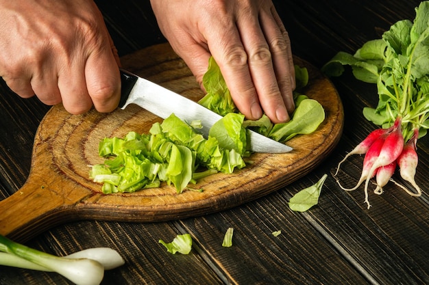 Chef-kok handen snijden groene slabladeren op een snijplank met een mes voor het bereiden van een vegetariër