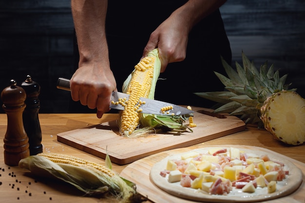 Chef-kok Hawaiiaanse pizza koken, verse maïs snijden