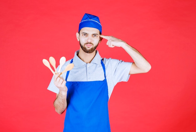 Chef-kok in blauwe schort die houten kleine lepels houdt en over keus denkt.