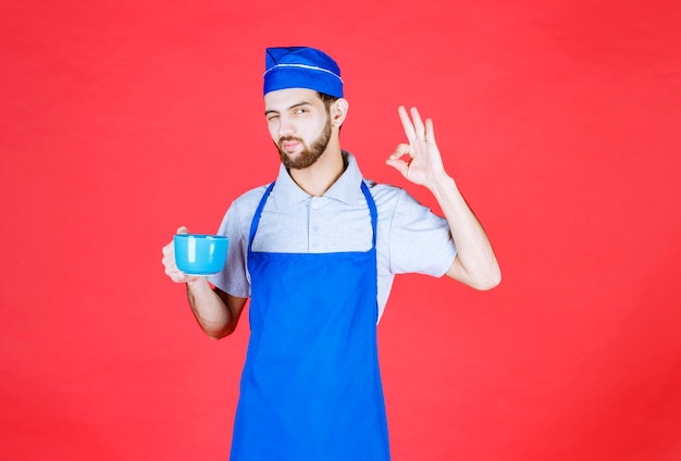 Chef-kok in blauwe schort met een blauwe keramische beker en genietend van de smaak van het product.