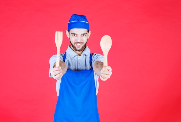 Chef-kok in blauwe schort met houten lepel en spatel.