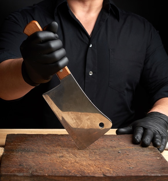 Chef-kok in een zwart shirt en zwarte latex handschoenen heeft een groot keukenmes