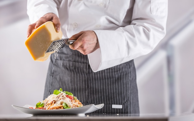 Chef-kok in restaurantkeuken bereidde Italiaanse maaltijdspaghetti en geraspte Parmezaanse kaas.