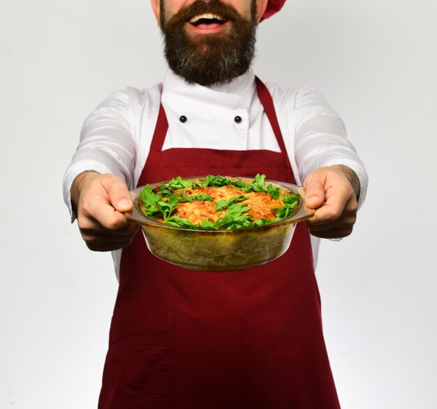 Chef-kok in uniform die een kom met aardappelschotel overhandigt