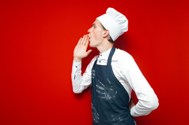 Chef-kok in uniform schreeuwt naar de zijkant op een rode geïsoleerde achtergrond keukenmedewerker adverteert kopieerruimte
