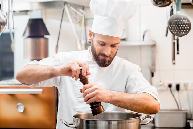 Chef-kok in uniforme pepersoep in het grote fornuis in de restaurantkeuken