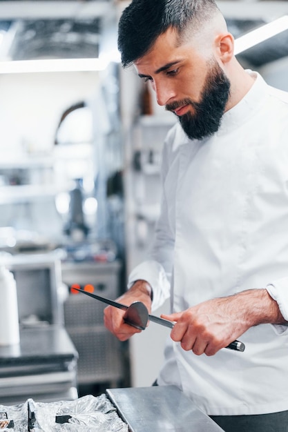 Chef-kok in wit uniform staat in de keuken met messen in handen