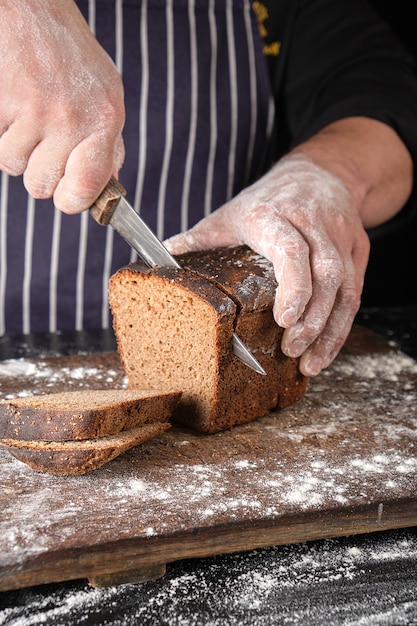 Chef-kok in zwart uniform houdt een keukenmes in zijn hand en snijdt brood af