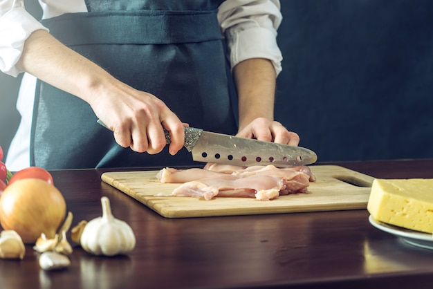 Chef-kok in zwarte schort kipfilet snijden