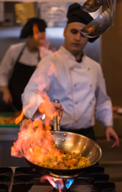 Chef-kok koken en flamberen op eten in de keuken van het restaurant