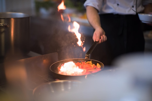 Chef-kok koken en flamberen op eten in de keuken van het restaurant