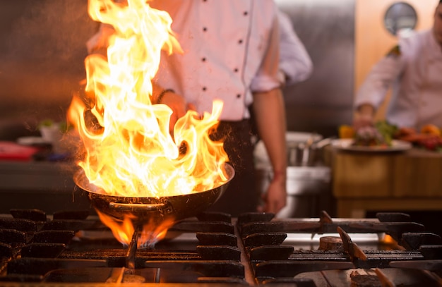 Chef-kok koken en flamberen op eten in de keuken van het restaurant