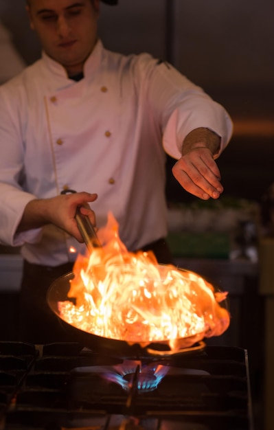 Chef-kok koken en flamberen op eten in de keuken van het restaurant