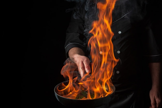 Chef-kok koken voedsel in pan met vuurvlam op zwarte achtergrond Restaurant en hotel dienstverleningsconcept