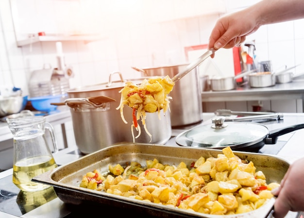 Chef-kok kookt gebakken aardappelen met stukjes vlees in de keuken van een restaurant