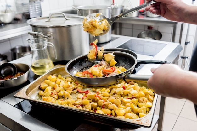 Chef-kok kookt gebakken aardappelen met stukjes vlees in de keuken van een restaurant