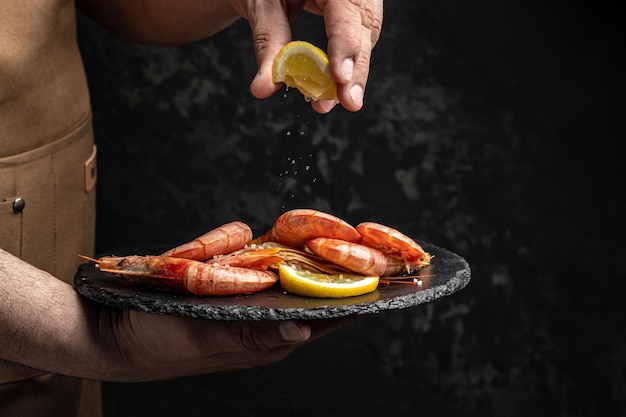 Chef-kok kookt heerlijke garnalen met kruiden Garnalen gebakken met spatten citroensap in een vriesbeweging op een donkere achtergrond Zeevruchtenvoorgerecht Culinair kookconcept