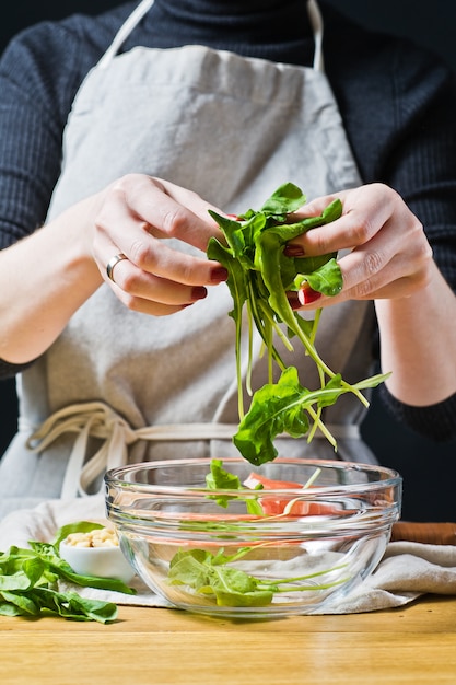 Chef-kok legt rucola-bladeren in een kom, het voorbereiden van een salade.