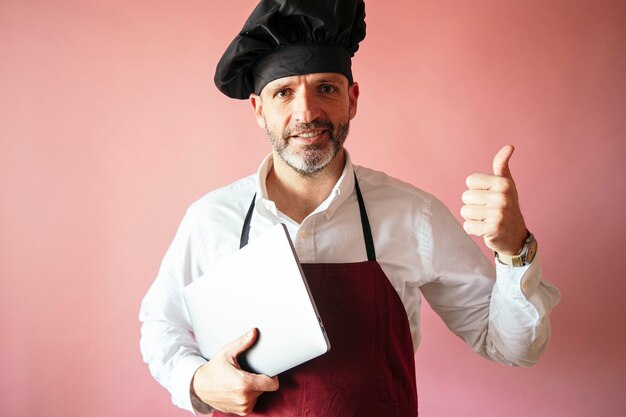 Chef-kok man met laptop met roze muur