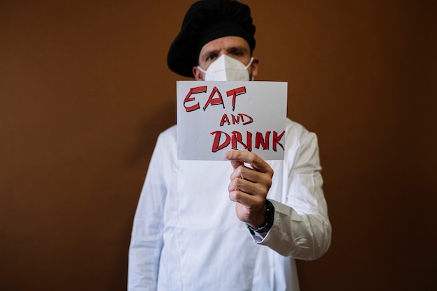 Chef-kok met een bordje met de tekst Eat and Drink, hij draagt een masker op zijn gezicht
