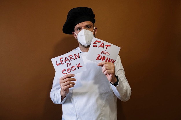 Chef-kok met een bordje met de tekst Eat and Drink, hij draagt een masker op zijn gezicht