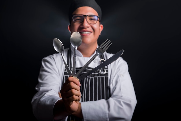 chef-kok met keukenbestek op de voorgrond selectieve focus met zwarte achtergrond