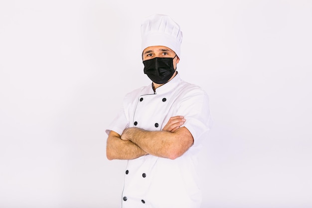 Chef-kok met keukenjas en hoed, met zwart masker, kruisende armen, op witte achtergrond