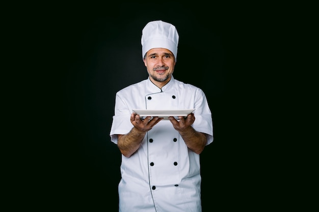 Chef-kok met kookjas en hoed, met een bord, op zwarte achtergrond