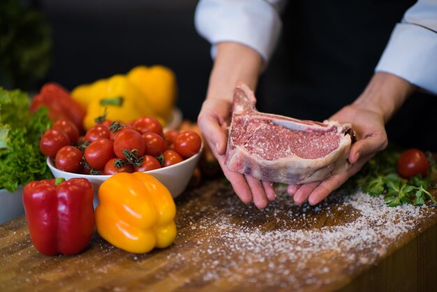 Chef-kok met sappige plak rauwe biefstuk met groenten rond op een houten tafel