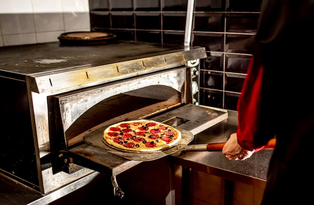 Foto chef-kok pizza aanbrengend oven om te koken